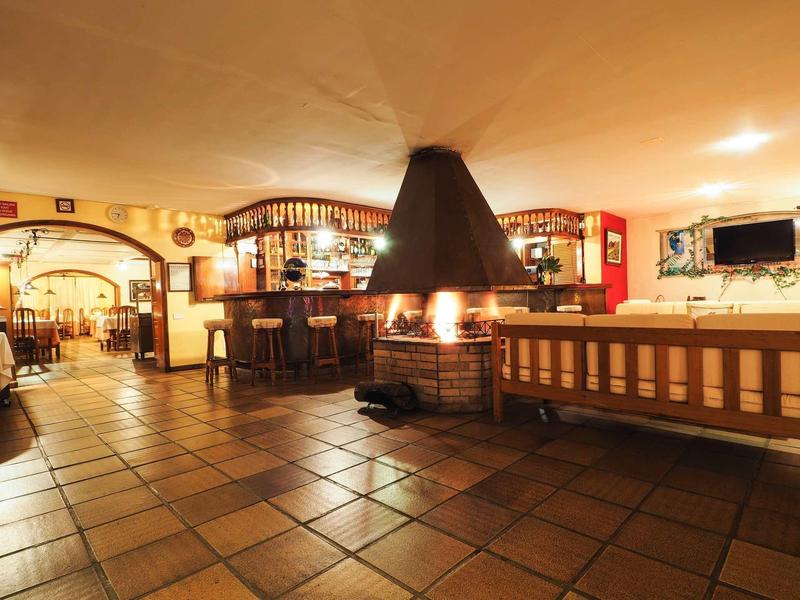 Bar cálida de hotel con chimenea, muebles de madera y suelo de baldosas en ambiente acogedor.