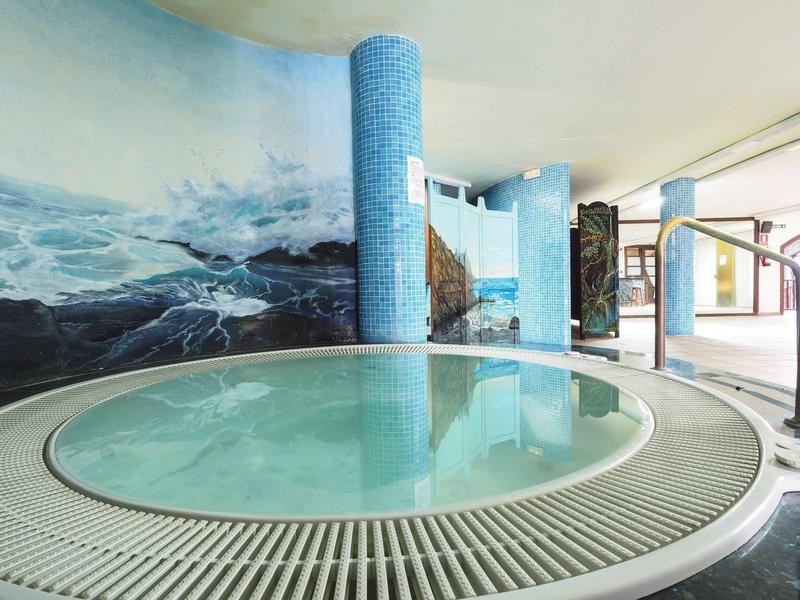 Jacuzzi moderno en área de spa bien iluminada con mural de mar.