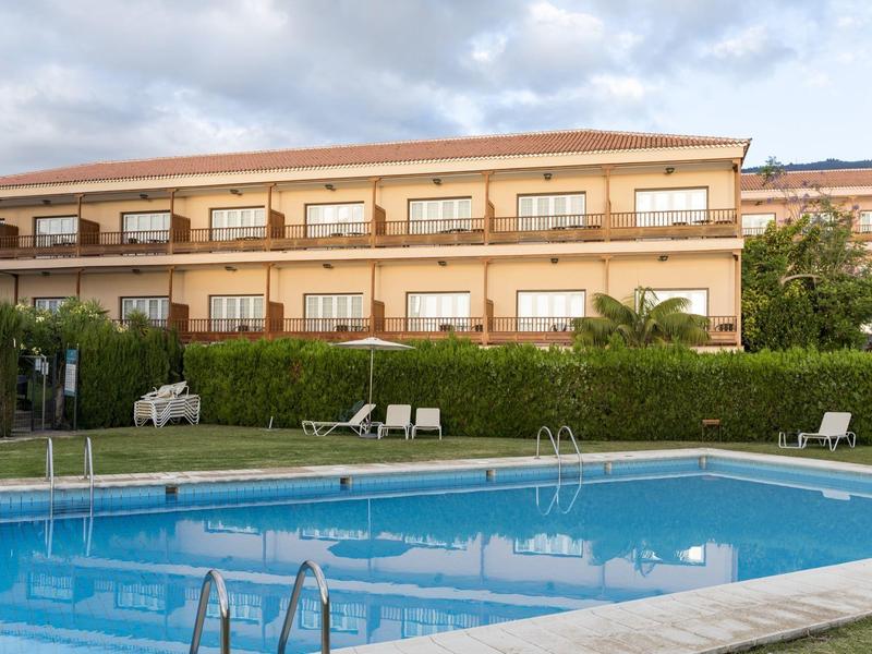 Spokojny basen przed hotelem z balkonami i leżakami.