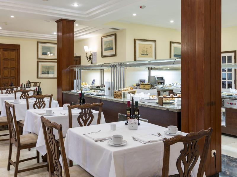 Elegancka jadalnia hotelowa z białymi stołami i bufetem w tle.