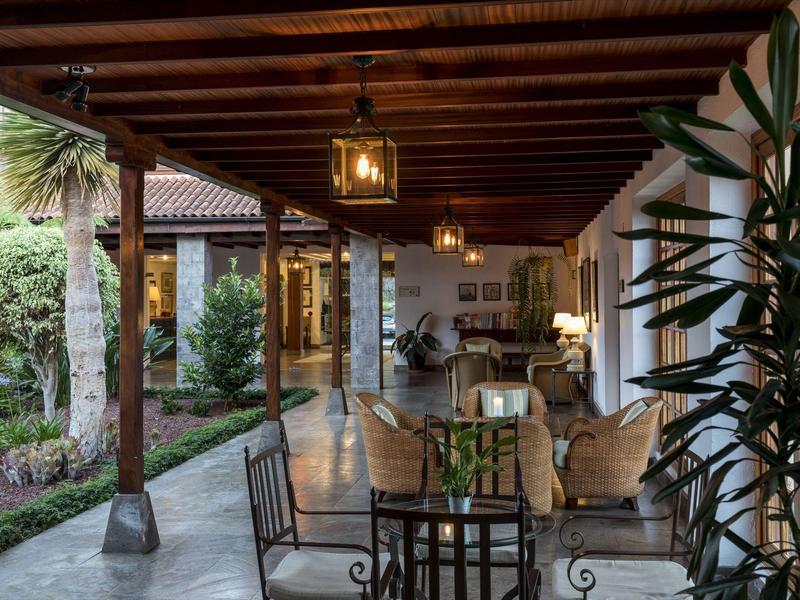 Zadaszony taras z metalowymi meblami i widokiem na bujny ogród.