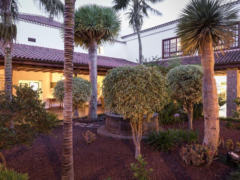 Starannie utrzymany ogród z palmami i krzewami przed domem w stylu śródziemnomorskim.
