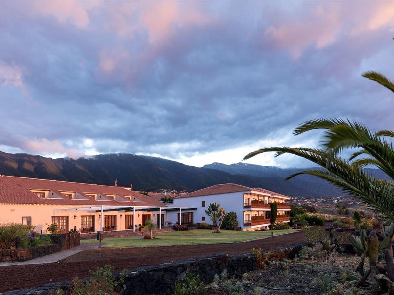 Hotel pod kolorowym niebem o zachodzie słońca z palmą na pierwszym planie.
