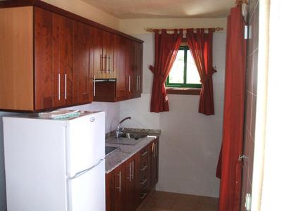 Kleine hotelkeuken met houten kasten, klein raam en witte koelkast.