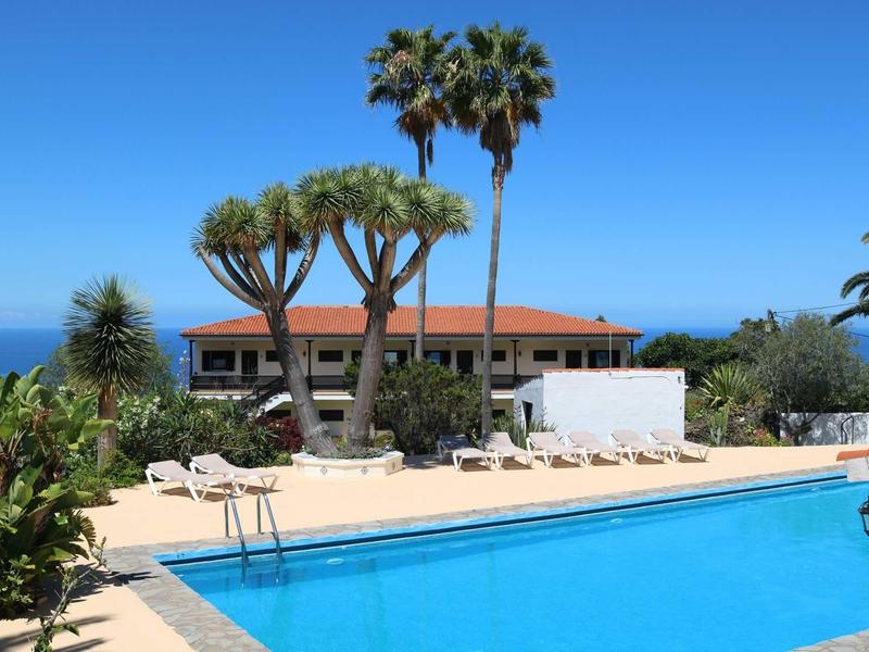 Piscina limpida davanti a un edificio con tetti rossi e alberi tropicali sotto un cielo azzurro