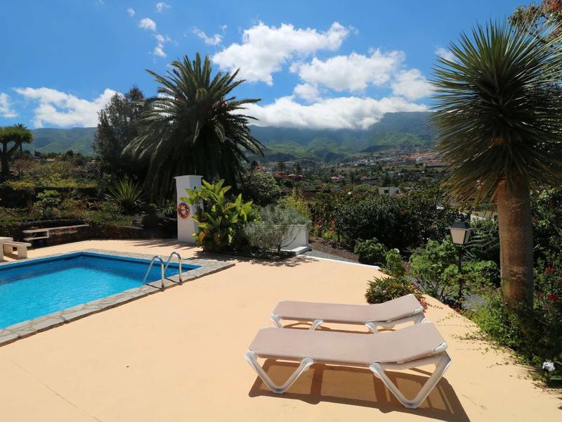 Area piscina con lettini e vista sulla città e sulle montagne sotto un cielo azzurro.