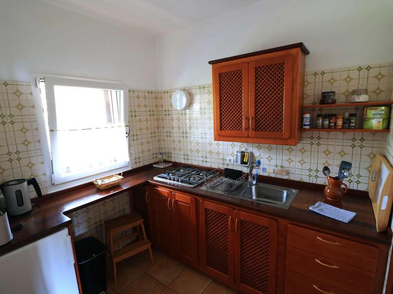 Piccola cucina con mobili in legno, lavello, fornello e finestra che lascia entrare la luce naturale.