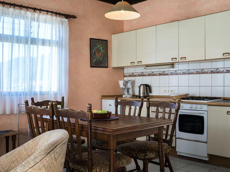 Kuchyně s dřevěným stolem, židlemi a spotřebiči před růžovými stěnami.