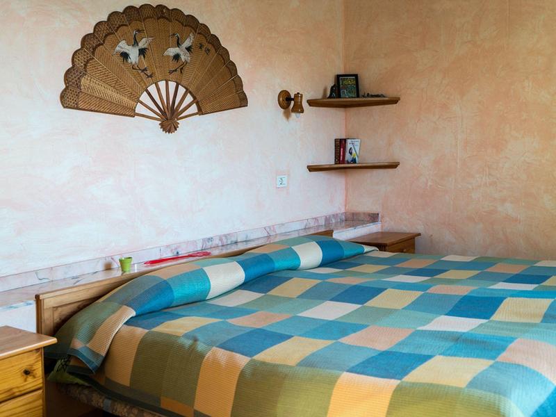 Ložnice s dřevěným rámem postele, barevnou kostkovanou přikrývkou a nástěnnou dekorací.