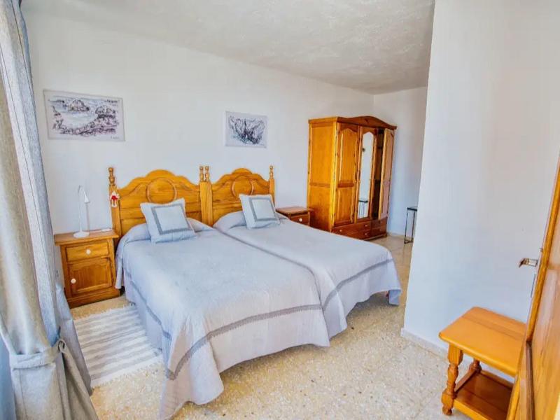 Světlá ložnice se dvěma jednolůžky, dřevěným nábytkem a oknem s závěsy.