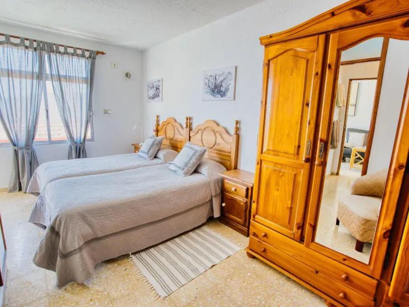 Světelná ložnice se dvěma jednolůžky, dřevěným nábytkem a oknem se šedými závěsy.