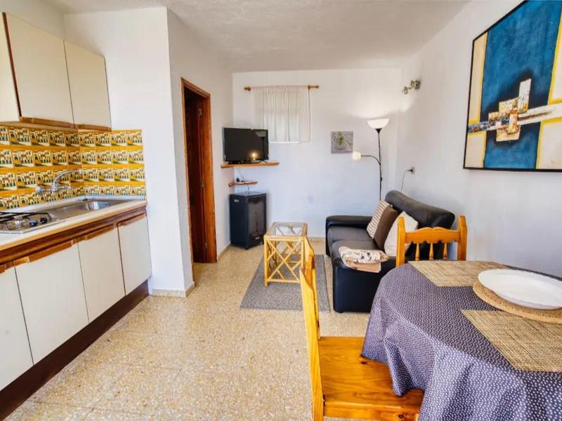 Pohodlný obývací prostor s malou kuchyní, jídelním stolem a pohovkou v rekreačním bytě.