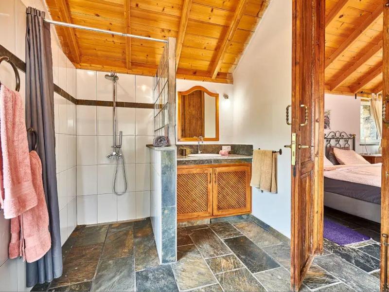 Pohodlná koupelna s otevřeným sprchovým koutem, dřevěným stropem a kamennou podlahou v rekreačním bytě.