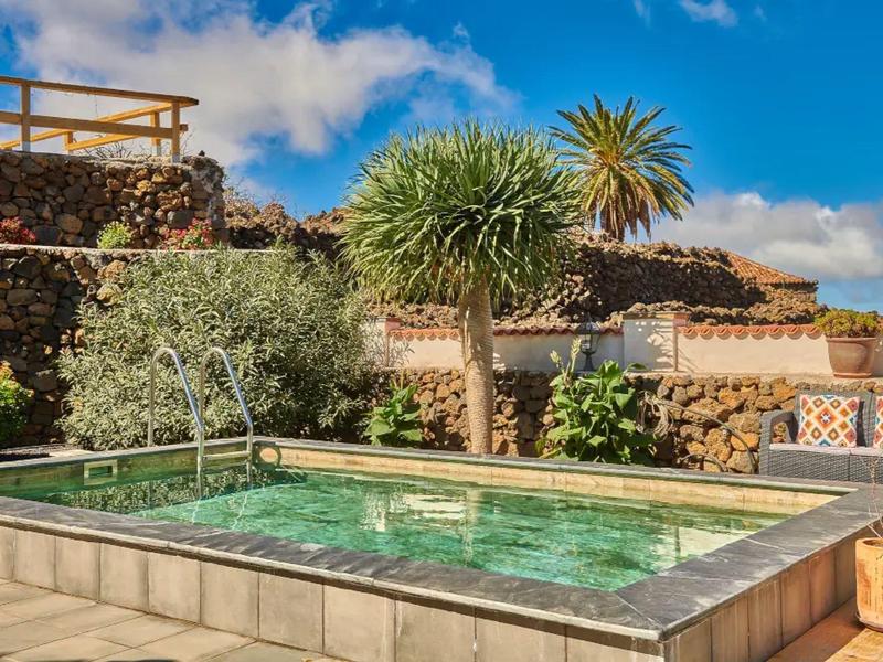 Malý bazén s průzračnou zelenou vodou vedle posezení a tropických rostlin.