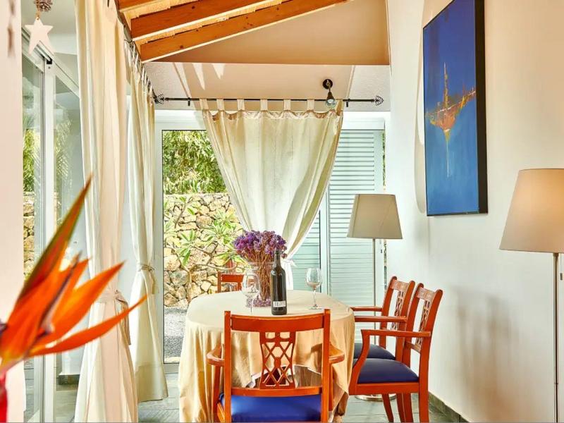 Světlý jídelní kout s dřevěnými židlemi, barevnou květinovou dekorací a bílými závěsy u skleněných oken.