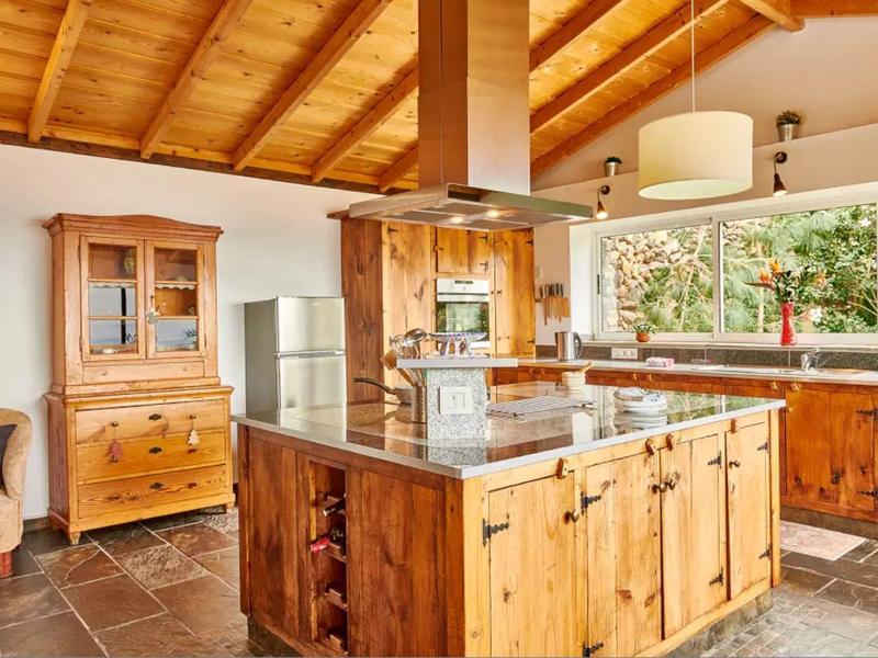 Kuchyně s velkým dřevěným ostrůvkem, dřevěným nábytkem a oknem s výhledem na zahradu.