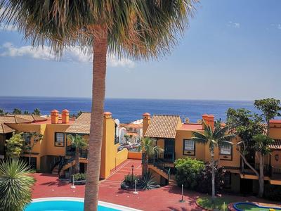 Ein Pool mit einem großen Felsen, umgeben von Wohnhäusern und einer Palme im Vordergrund.