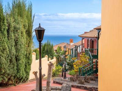 Blick auf einen Weg mit Laternen, umgeben von Gebäuden und Grün mit Meer im Hintergrund.