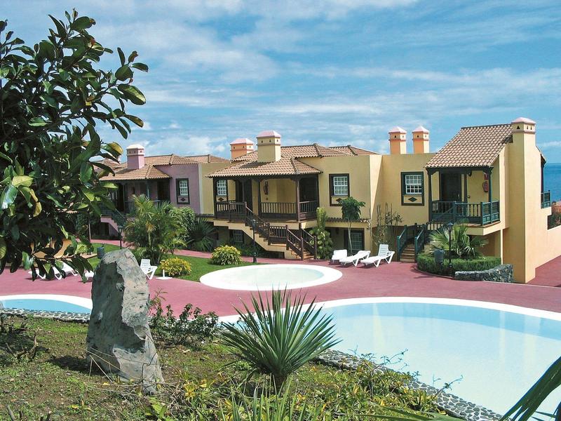 Wohnhaus mit Garten, Pool und Pflanzen unter blauem Himmel, klare helle Farben.
