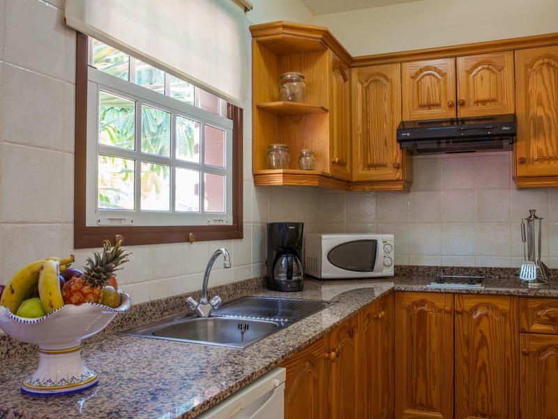 Kleine Küche mit Holzmöbeln, Granitarbeitsplatten, Fenster, Obstschale, Kaffeemaschine und Mikrowelle.