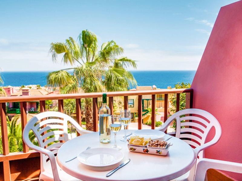 Terrasse mit Tisch, Stühlen, Essen und Blick auf das Meer und Palmen bei klarem Himmel.