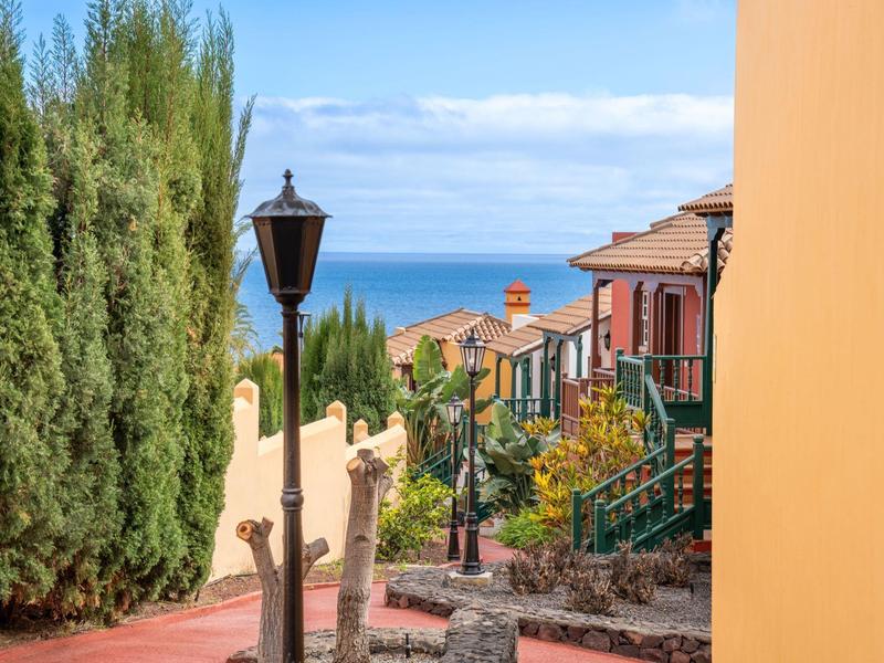 Schmale Gasse mit Laternen und Häusern mit Blick auf das Meer unter blauem Himmel.