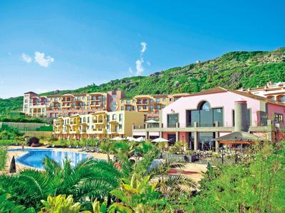 Hotel s bazénem před zeleným kopcem pod modrou oblohou