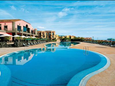 Großer geschwungener Hotelpool mit Liegestühlen und Gebäuden im Hintergrund bei klarem Himmel.