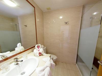 Baño luminoso con lavabo, espejo grande y toalla doblada en forma de corazón.