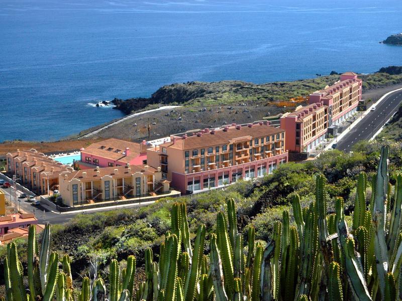 Complejo hotelero en la costa con paisaje árido y cactus en primer plano.