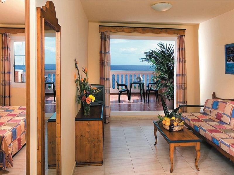 Habitación de hotel con balcón y vista al mar, equipada con cama, sofá y mesa.