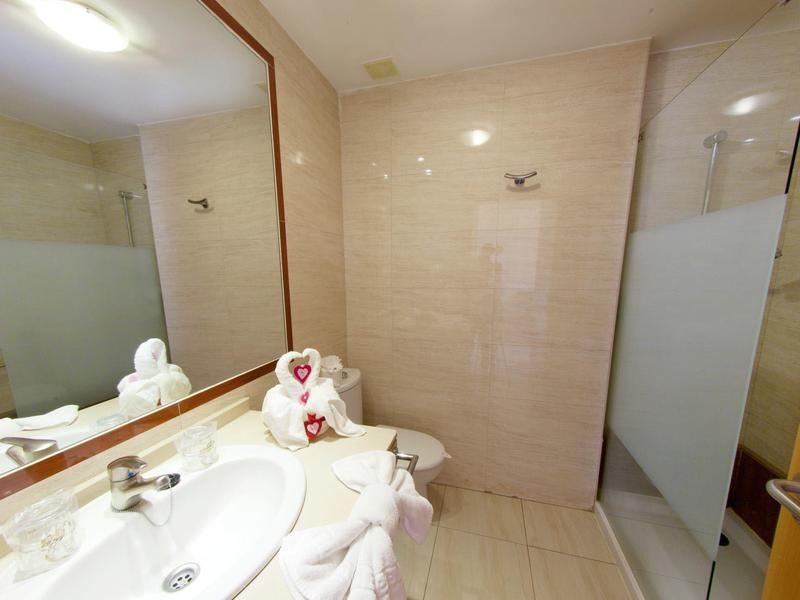 Baño luminoso con lavabo, espejo grande y toalla doblada en forma de corazón.