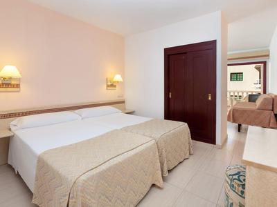 Bright hotel room with two beds, wardrobe, and view of seating area and TV.