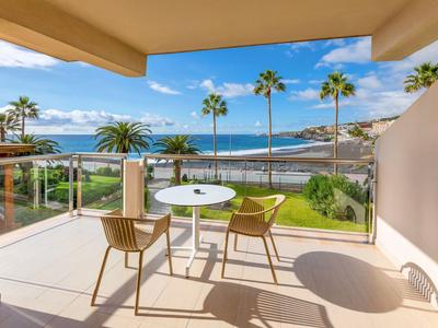 Balcon avec deux chaises et une table donnant sur la mer et les palmiers.