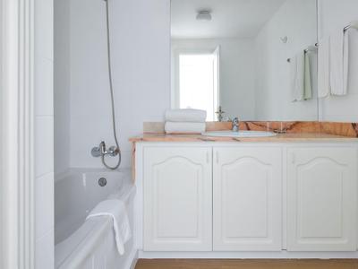 Bright bathroom with white bathtub and sink on wooden countertop.