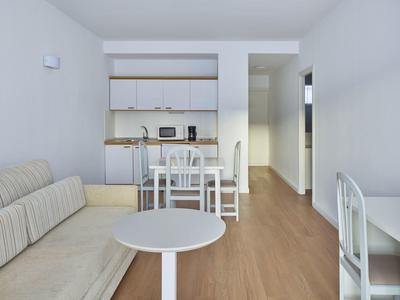 Bright living room with sofa, round coffee table, dining table, and open kitchen with white cabinets.