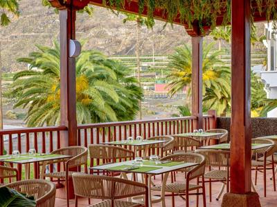 Covered terrace with tables and chairs, view of palm trees and mountains in the background.