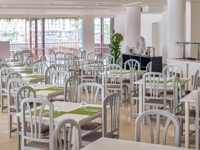 Bright, modern dining area with white chairs and tables, green placemats, and large windows.