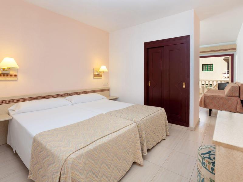 Bright hotel room with two beds, wardrobe, and view of seating area and TV.