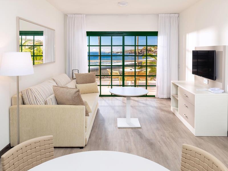 Bright living room with sofa, TV, and large window overlooking the sea.