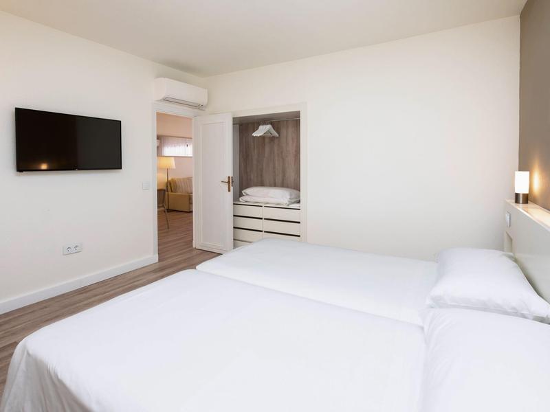 Modern hotel room with two beds, wall-mounted TV, and view into the bathroom.