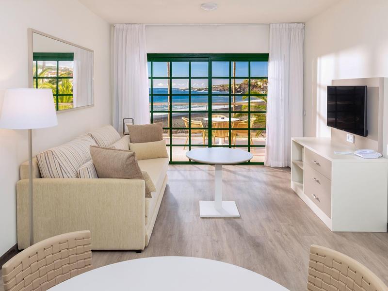 Bright living room with sofa, TV, and large window overlooking the beach.