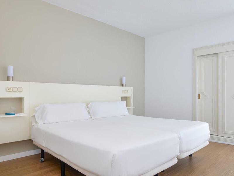 Bright, modern hotel room with two single beds, bedside lamps, and a white wardrobe.