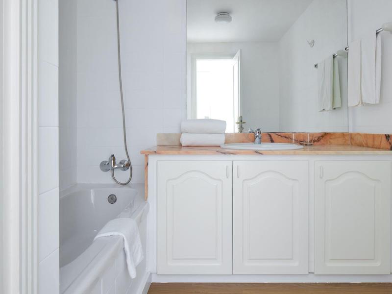 Bright bathroom with white bathtub and sink on wooden countertop.