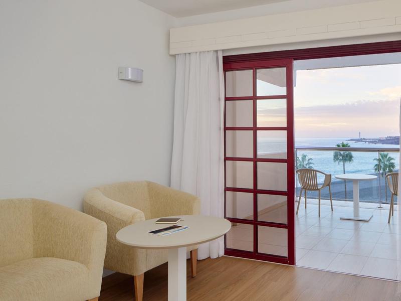 Two cream armchairs and a small round table in front of a door overlooking the terrace and the sea.