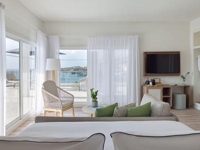 Chambre d'hôtel moderne avec vue sur la mer, deux lits, coin salon et télévision.