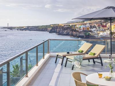 Balcon avec chaises longues et table surplombant la mer et une ville côtière.