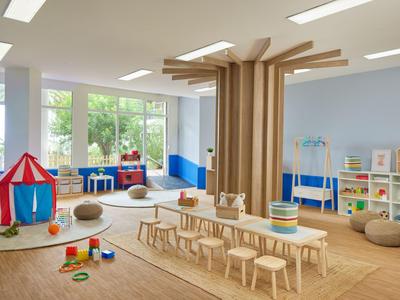 Salle de jeux lumineuse pour enfants avec tables, chaises, jouets et grandes fenêtres.