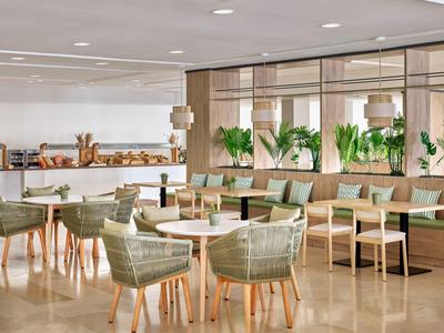 Café moderne et lumineux avec des chaises vertes, des tables en bois et un comptoir avec des pâtisseries.