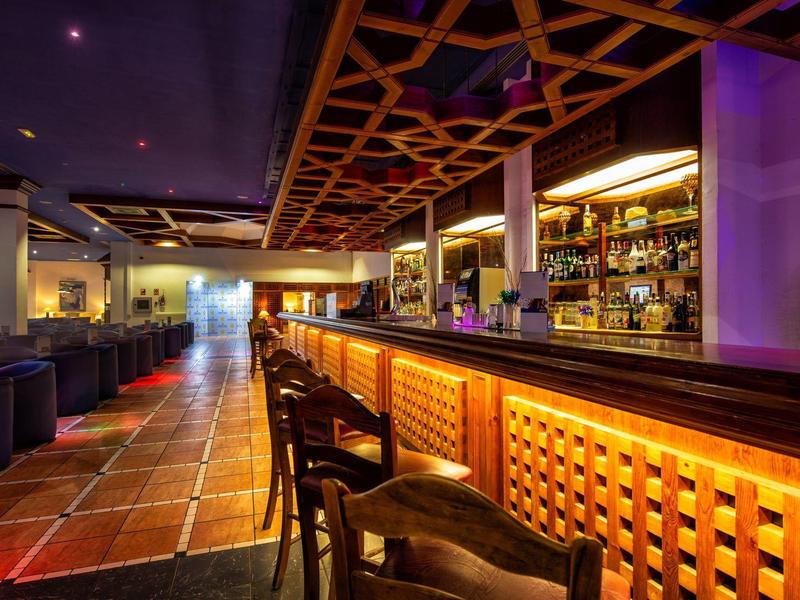 Moderner Barraum mit langer Holztheke, Hockern und gemütlicher Sitzfläche mit gedämpftem Licht.